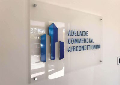 A custom made glass rectangular sign with vinyl cut lettering and 3D lettering hung in an office reception area